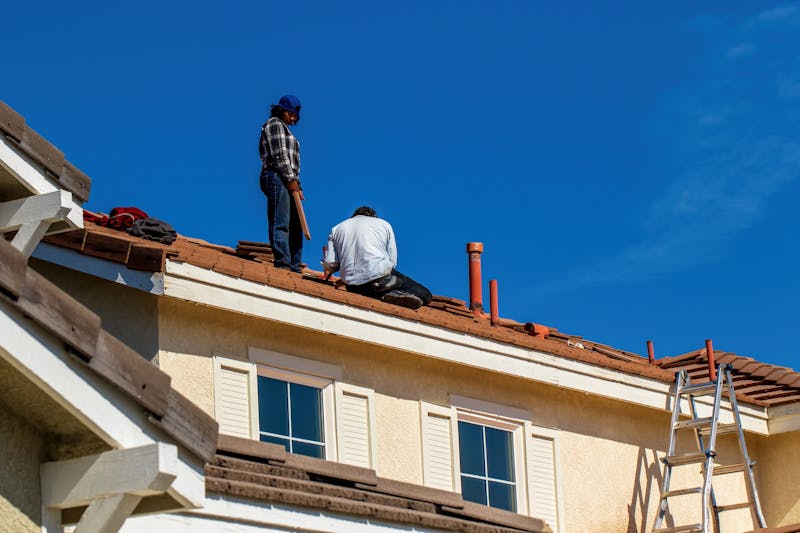 Gutter Repair — Roof construction scene with workers on a tiled roof, captured under a clear blue sky.
